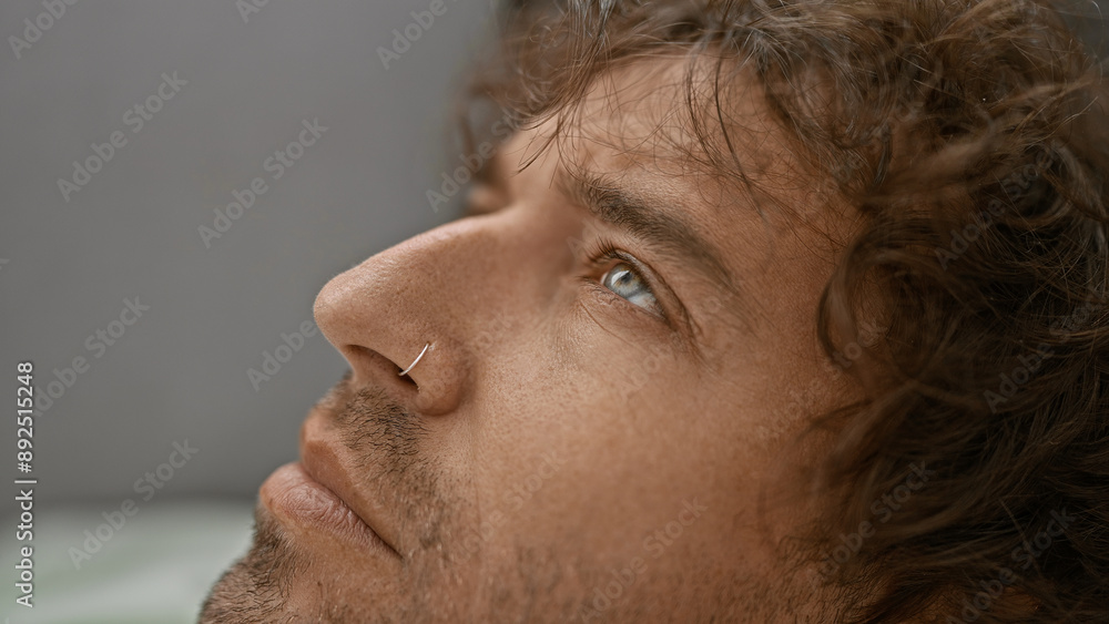 Fototapeta premium Handsome hispanic man with green eyes and beard lying on a sofa indoors, gazing upward thoughtfully.