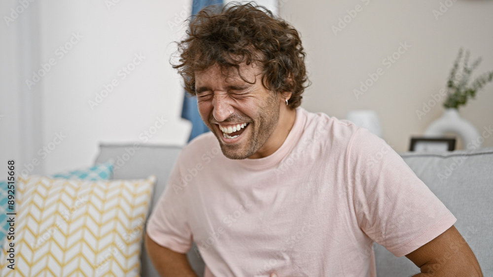 Laughing hispanic man in a light-filled cozy living room, feeling joyful, captured in a close-up portrait. Laughing hispanic man in a light-filled cozy living room, feeling joyful, captured in a close-up portrait.