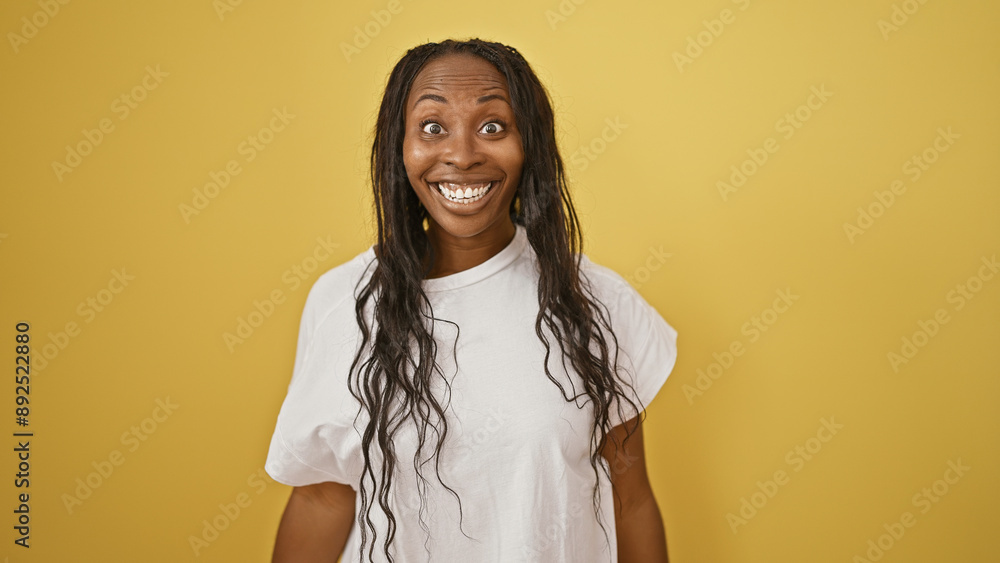 Smiling young african american woman with curly hair against yellow isolated background in a casual white shirt. Smiling young african american woman with curly hair against yellow isolated background in a casual white shirt.