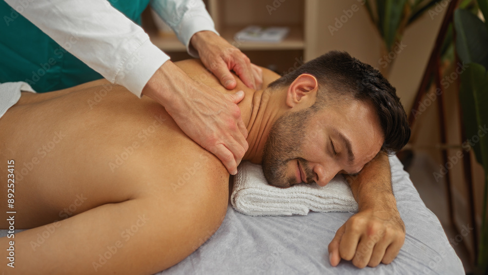 Man receiving relaxing massage from therapist in wellness spa center Man receiving relaxing massage from therapist in wellness spa center