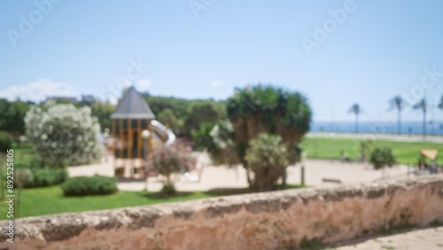 Blurred sunny mallorca outdoor scene with playground surrounded by lush greenery and defocused trees under a clear blue sky