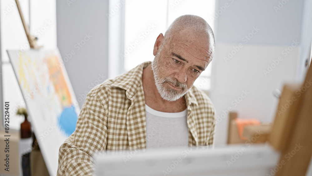 Fototapeta premium A senior man with grey beard engaged in painting indoors, concentrated on his creative hobby.