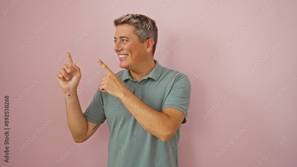 Young man smiling and pointing to the side against an isolated pink background Young man smiling and pointing to the side against an isolated pink background