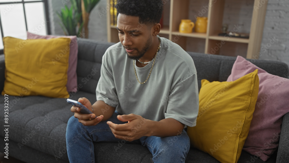 Pensive african american man using smartphone on couch with colorful pillows in living room Pensive african american man using smartphone on couch with colorful pillows in living room
