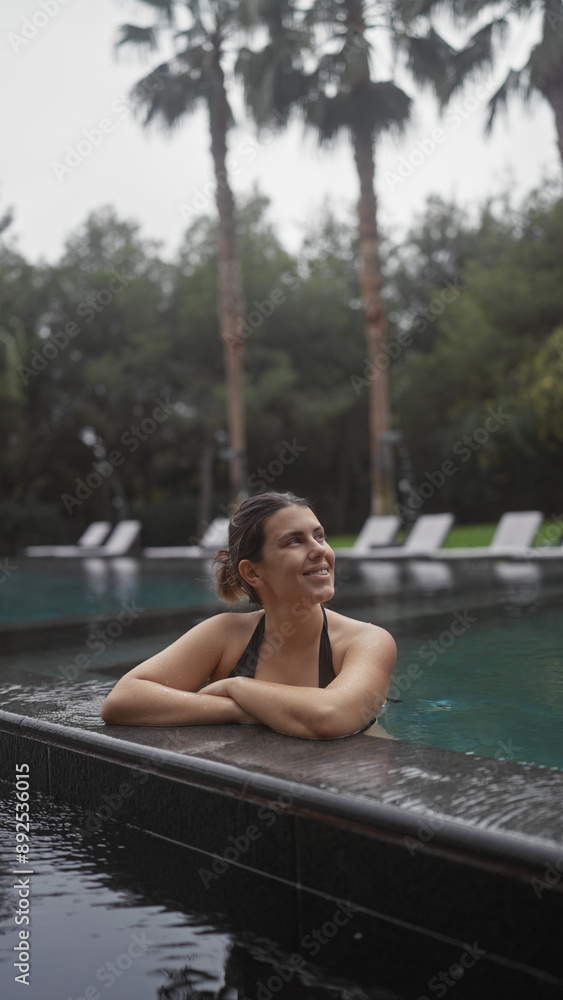 Smiling young woman relaxing in a luxurious bali resort swimming pool surrounded by tropical palms. Smiling young woman relaxing in a luxurious bali resort swimming pool surrounded by tropical palms.