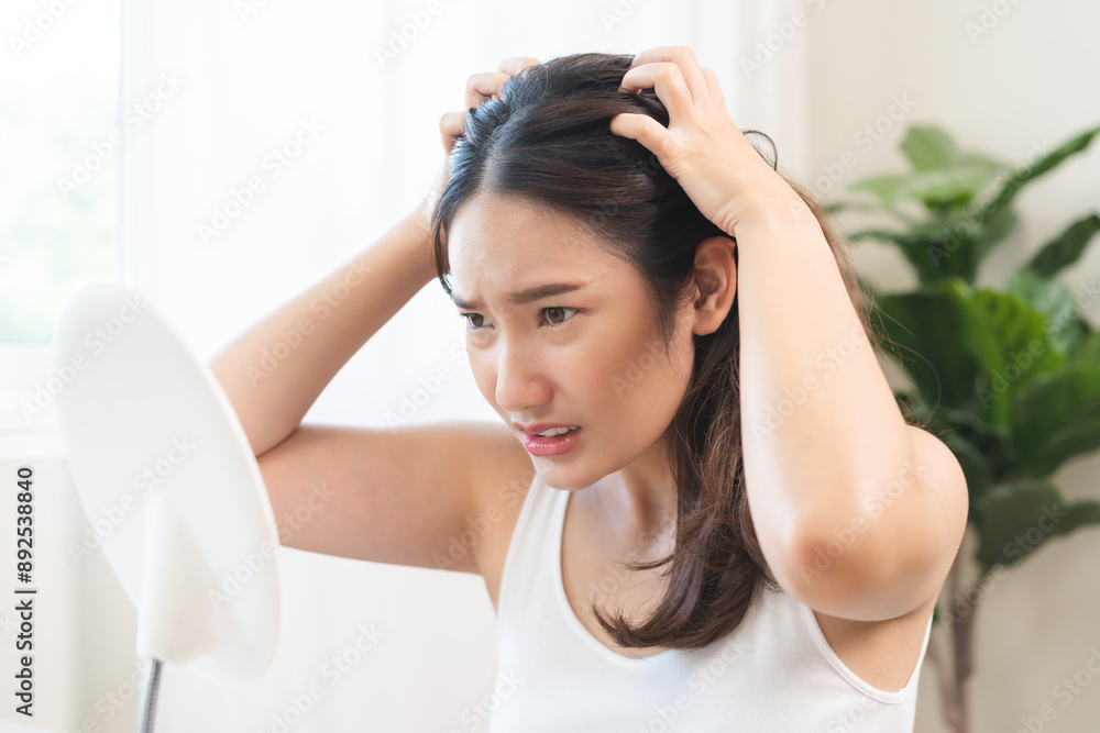 Damaged Hair symptom, face serious asian young woman, girl worry about balding, looking at scalp in mirror, hand in break into front hair loss, thin problem. Health care treatment for beauty concept. Damaged Hair symptom, face serious asian young woman, girl worry about balding, looking at scalp in mirror, hand in break into front hair loss, thin problem. Health care treatment for beauty concept.