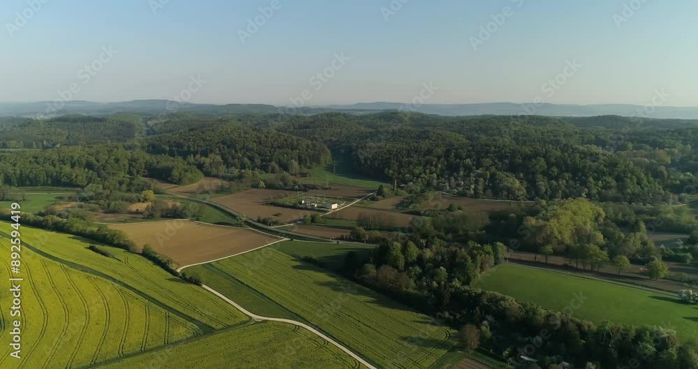 A drone camera captures a scenic view of rolling hills, lush green fields, and dense forests in a rural area of Germany. The sunlight casts long shadows across the landscape, highlighting the texture A drone camera captures a scenic view of rolling hills, lush green fields, and dense forests in a rural area of Germany. The sunlight casts long shadows across the landscape, highlighting the texture