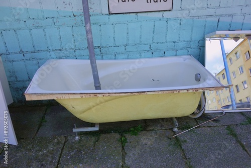 A bathtub from an apartment building thrown out next to a dumpster building. Old damaged bathtub near the dumpster building and a mirror with the reflection of old apartment blocks. photo