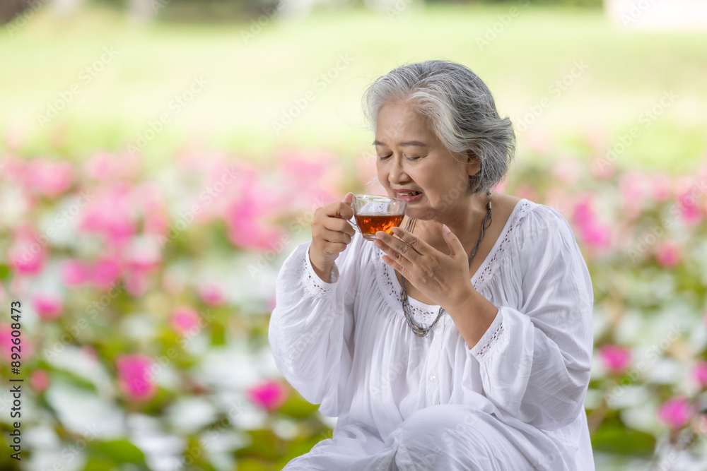 Fototapeta premium Elderly Woman Enjoying a Cup of Tea in a Lush Garden with Pink Water Lilies, Embracing Tranquility and Relaxation in Nature While Wearing a White Outfit
