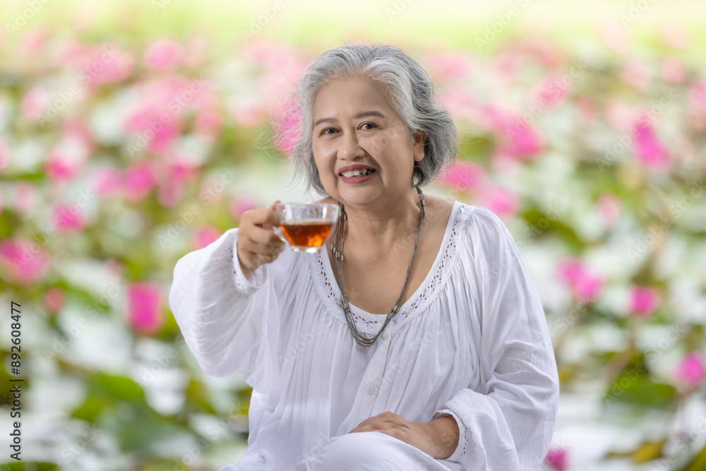 Fototapeta premium Elderly Woman Enjoying a Cup of Tea in a Lush Garden with Pink Water Lilies, Embracing Tranquility and Relaxation in Nature While Wearing a White Outfit