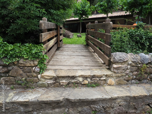 pequeño puente de madera para cruzar el arroyo de la villa medieval de rivert, al fondo una área recreativa para pasar una feliz tarde de verano, lérida, españa, europa