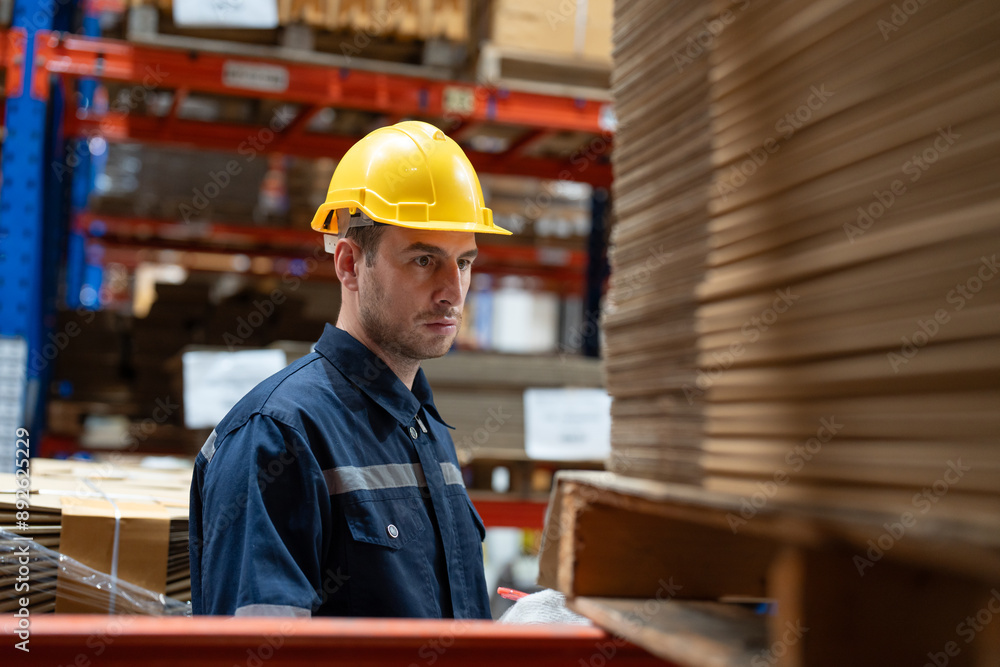 Man warehouse worker wearing uniform and helmet safety standing with clipboard for checking stock products on shelves in warehouse Man warehouse worker wearing uniform and helmet safety standing with clipboard for checking stock products on shelves in warehouse
