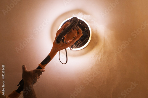Konstfotografi A plasterer's hand and a grinder for plaster and putty at work with a backlight