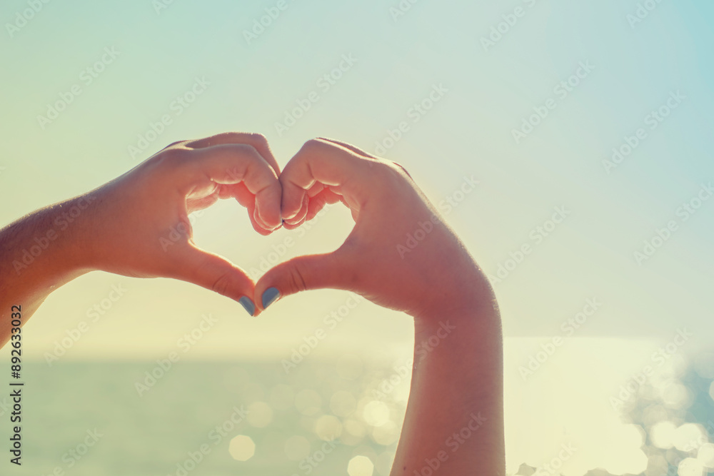 Girl's hands in the shape of a heart against the background of the sea, close-up. Hands in the shape of a love heart. Romantic background Girl's hands in the shape of a heart against the background of the sea, close-up. Hands in the shape of a love heart. Romantic background