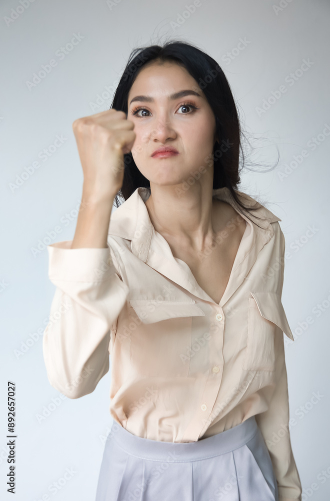 Angry upset unhappy young adult Asian woman with angry or furious expression, raising her threatening fist, ready to fight and punch right away Angry upset unhappy young adult Asian woman with angry or furious expression, raising her threatening fist, ready to fight and punch right away