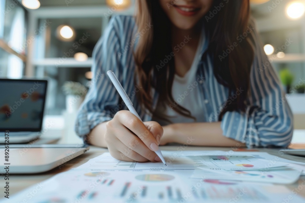 Smiling Asian Woman Analyzing Financial Data Charts on Desk Business Strategy, White Pen in Office Setting Smiling Asian Woman Analyzing Financial Data Charts on Desk Business Strategy, White Pen in Office Setting