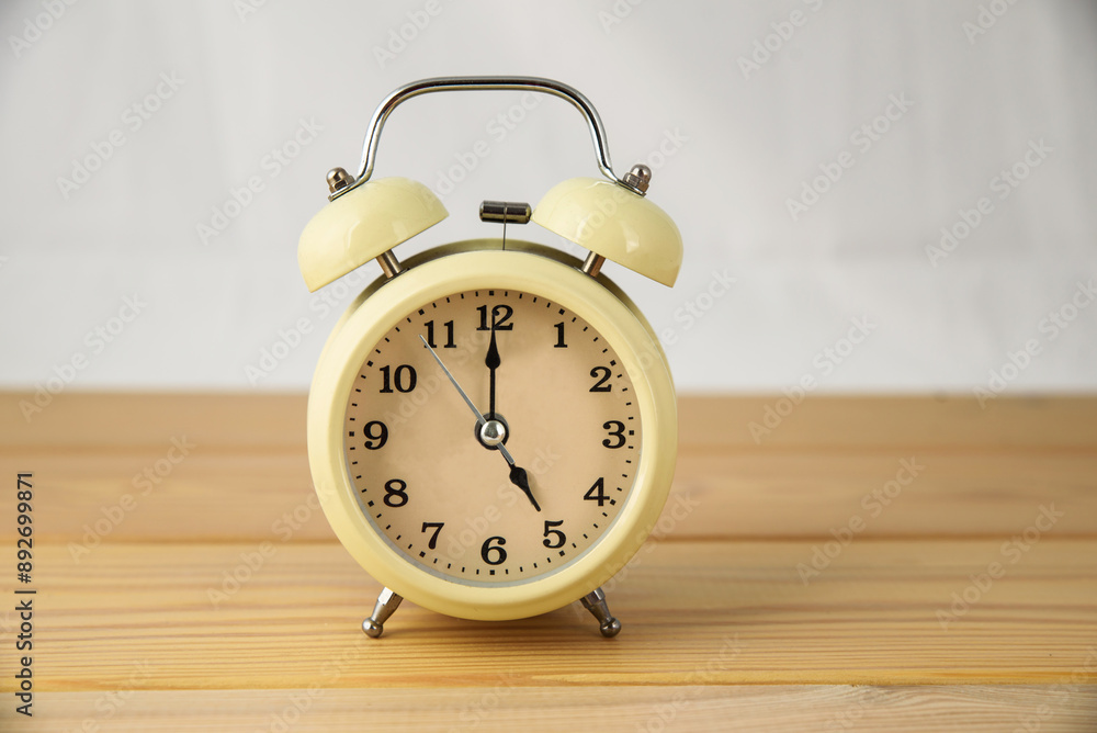 A large analog alarm clock on a wooden table. The idea of deadlines and hard work. 5 o'clock in the afternoon A large analog alarm clock on a wooden table. The idea of deadlines and hard work. 5 o'clock in the afternoon