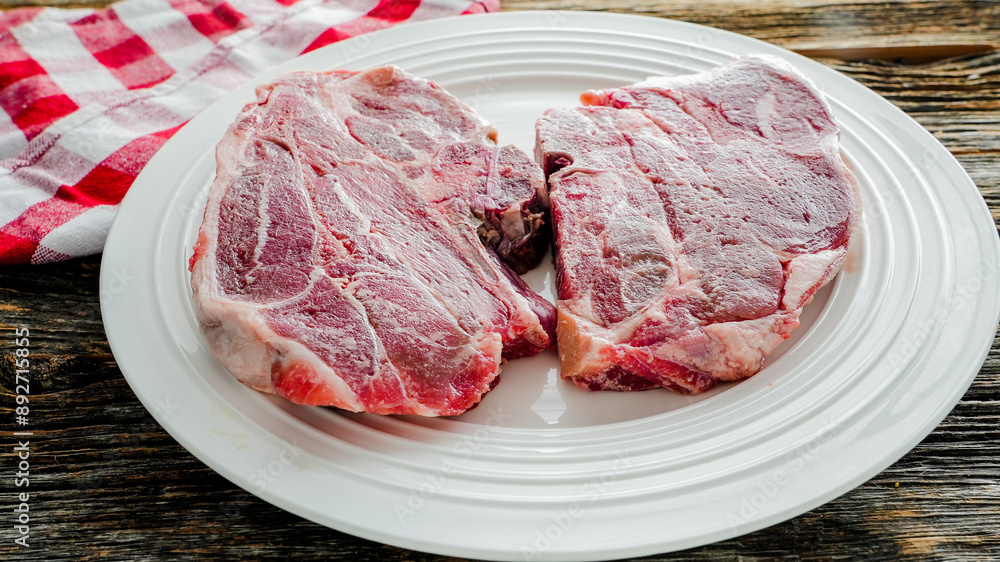 Two raw frozen lamb chops on white plate with red checkered napkin Two raw frozen lamb chops on white plate with red checkered napkin