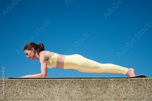Tableau sur toile Sporty woman doing a forearm plank exercise outdoors, wearing yellow sports clot