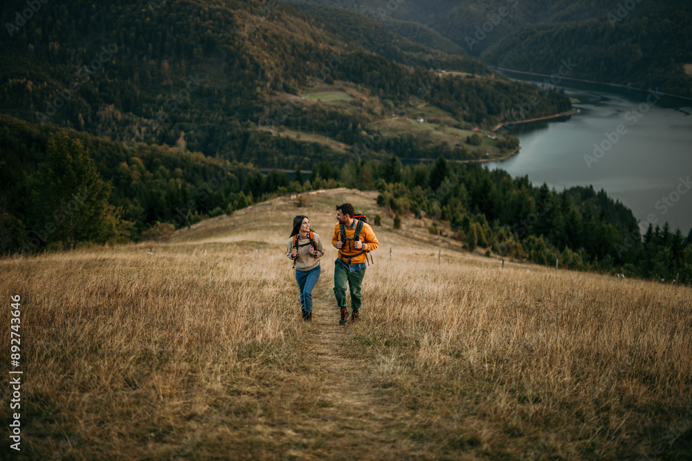 A couple explores nature, enjoying the beauty of an evening hike. The lake visible in the background A couple explores nature, enjoying the beauty of an evening hike. The lake visible in the background