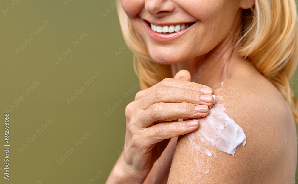 A woman is smiling as she applies skincare cream on her shoulder A woman is smiling as she applies skincare cream on her shoulder