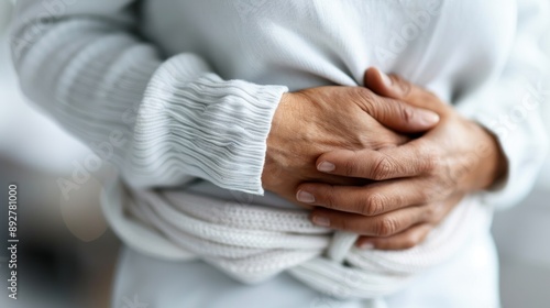 A close-up image of a person wearing a white sweater clutching their stomach in pain, vividly conveying the sensation of discomfort and ailment through their hand gesture and posture.