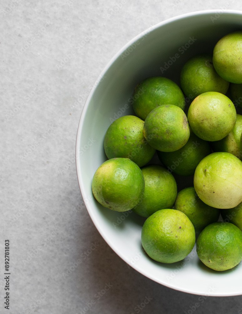 Overhead view of green limes in a white ceramic bowl, top view of organic limes in a white bowl Overhead view of green limes in a white ceramic bowl, top view of organic limes in a white bowl