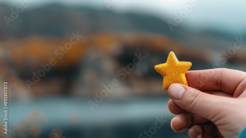 A hand holding a small yellow star against a blurred natural background. Starred rating symbol for tourist attractions, exploration, and wonder, highlighting a playful and adventurous spirit.