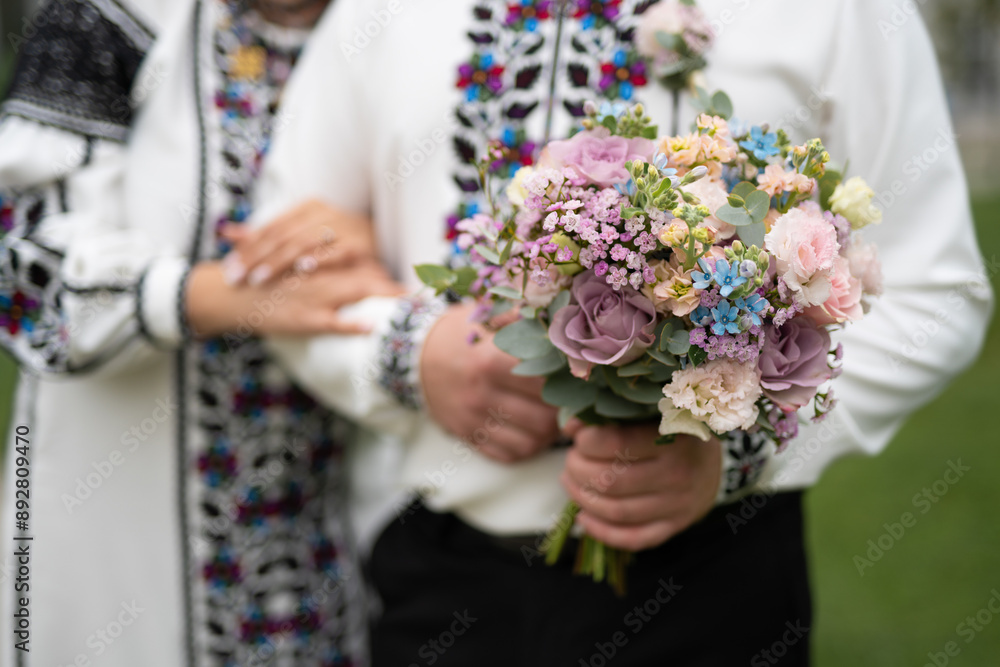 the bride and groom are holding hands with a bouquet of flowers and in traditional Ukrainian clothes