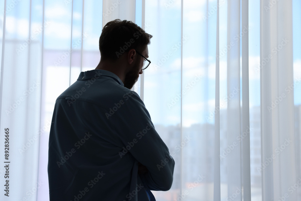 Loneliness concept. Sad man near window at home, back view. Space for text Loneliness concept. Sad man near window at home, back view. Space for text