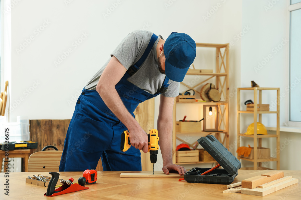 Craftsman working with drill at wooden table in workshop Craftsman working with drill at wooden table in workshop