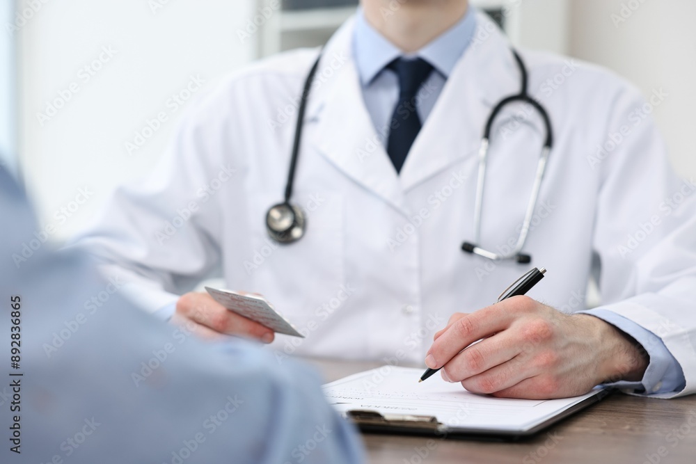 Doctor writing prescription for patient at wooden table in clinic, closeup Doctor writing prescription for patient at wooden table in clinic, closeup