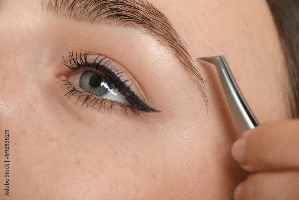Naklejka premium Beautician plucking young woman's eyebrow, closeup view