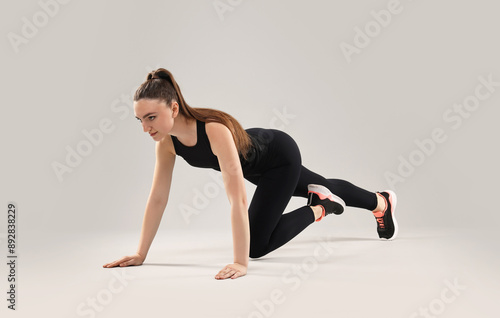 Young woman doing aerobic exercise on light background