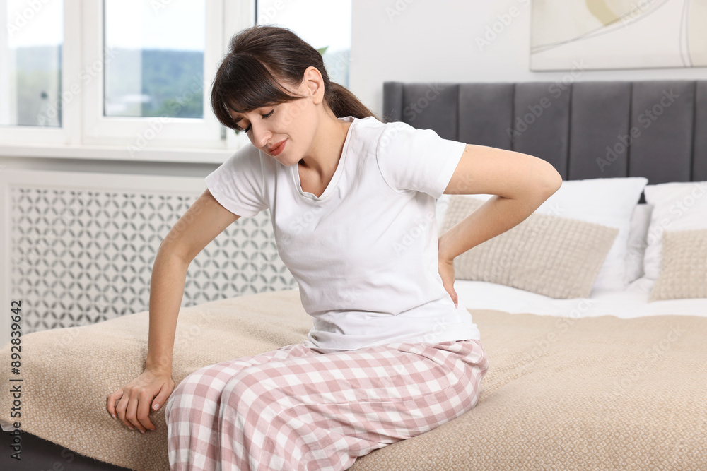 Upset woman suffering from back pain on bed at home Upset woman suffering from back pain on bed at home