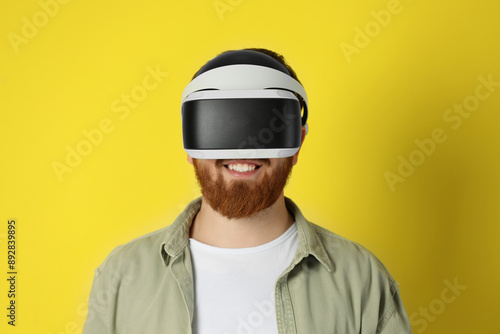 Smiling man using virtual reality headset on pale yellow background