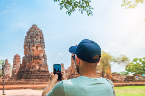 Canvas Print Man tourist taking picture of ancient Wat Mahathat temple with smartphone in Ayutthaya historical park, Thailand