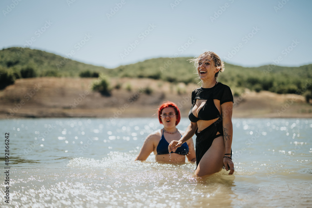 Fototapeta premium Two women smiling and enjoying a sunny day while swimming in a beautiful lake surrounded by hills.