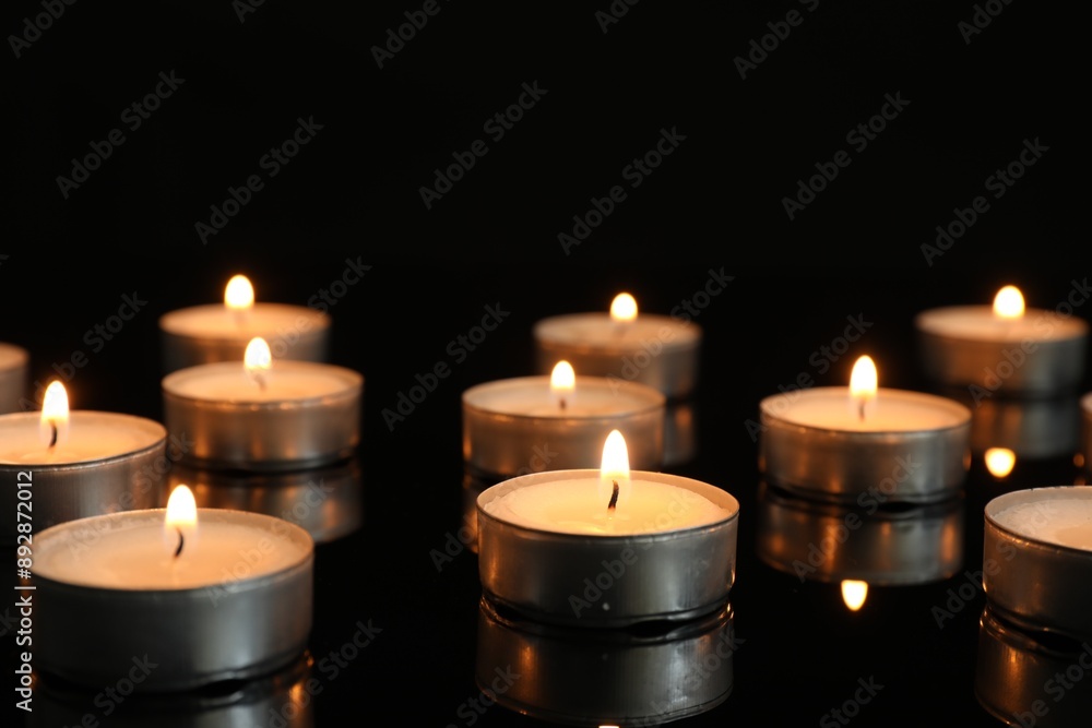 Many burning tealight candles on mirror surface against black background Many burning tealight candles on mirror surface against black background