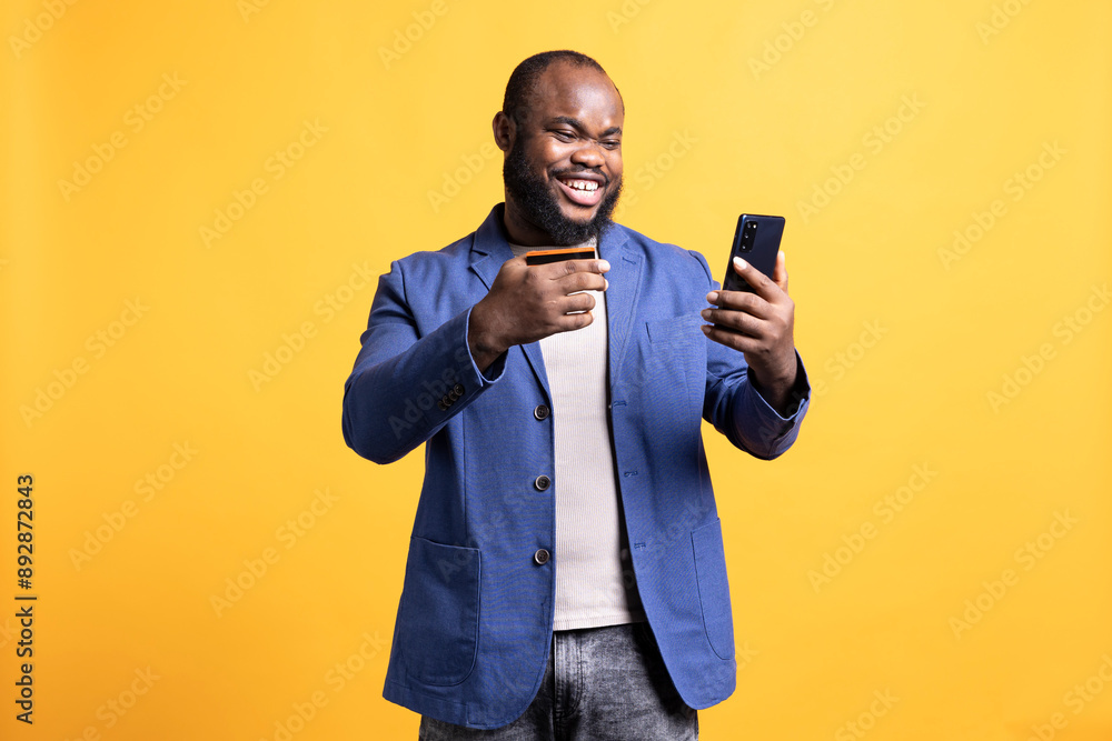Upbeat man giddying in excitement while adding payment method on phone, enjoying himself, studio background. Ecstatic person satisfying urges with internet shopping, typing credit card information Upbeat man giddying in excitement while adding payment method on phone, enjoying himself, studio background. Ecstatic person satisfying urges with internet shopping, typing credit card information