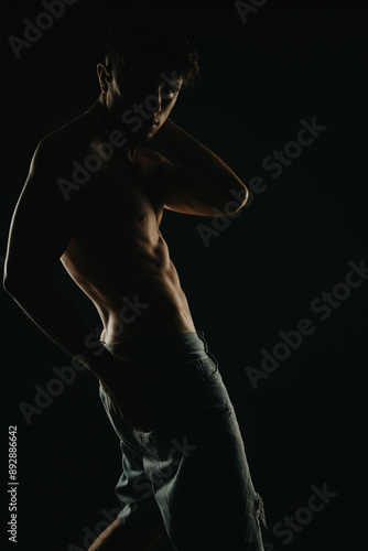 Dramatic silhouette of a shirtless man highlighting his muscular physique in low light against a dark background © qunica.com
