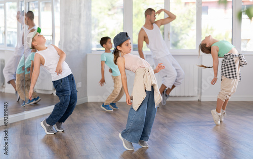 Energetic preteen girl practicing hip hop choreography in well-lit dance studio alongside peers and young male instructor photo