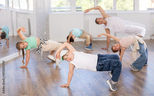 Emotional tween boy dancer rehearsing modern krump dance moves during group workout in kids studio under guidance of male instructor photo