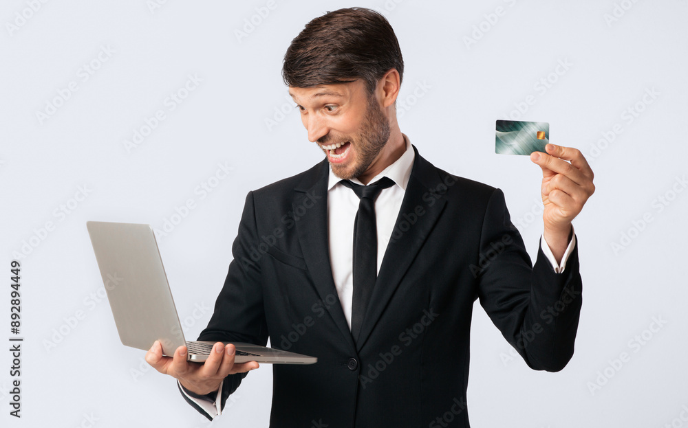 E-Commerce. Excited Businessman Holding Credit Card And Laptop Standing On White Background. Studio Shot, Isolated