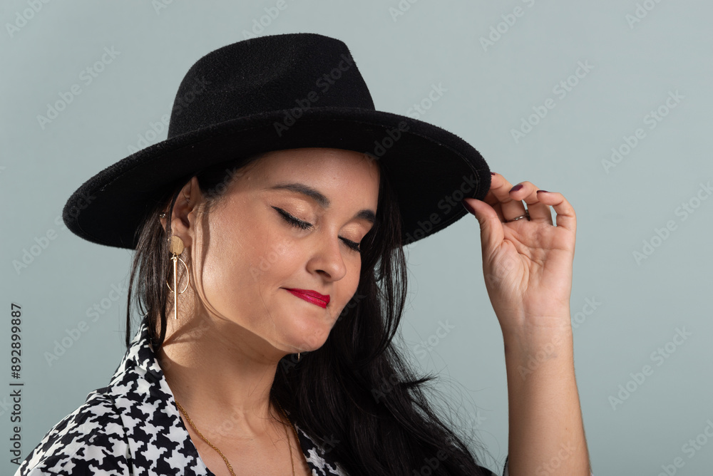 Close-up portrait of smiling beautiful woman with black hair wearing a black hat posing for photo in black and white outfit.