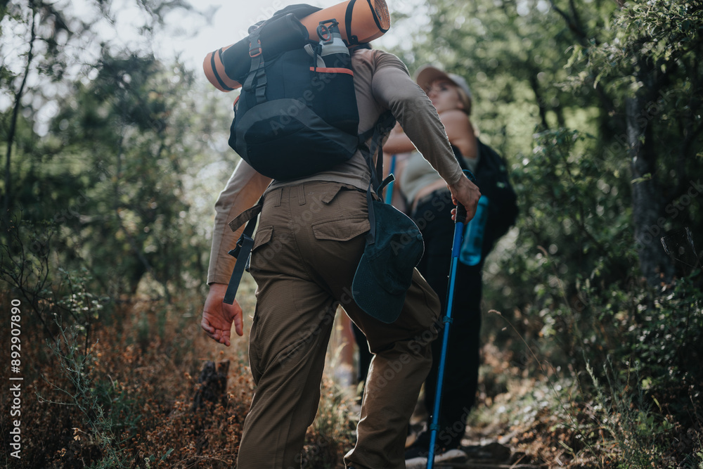 Two backpackers hiking through a dense forest trail, equipped with trekking poles and camping gear, enjoying an outdoor adventure. Two backpackers hiking through a dense forest trail, equipped with trekking poles and camping gear, enjoying an outdoor adventure.