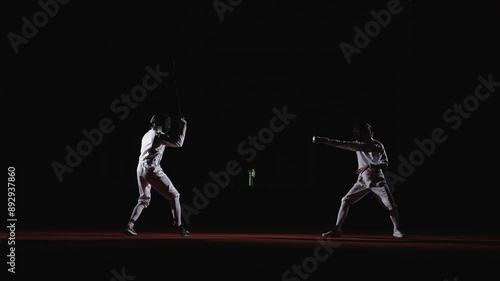 Sparring Of Two Professional Fencers On Fencing Rack, Full-Length Shot With Men Fighting In Darkness photo