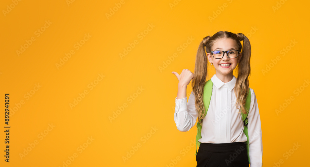 Back-To-School Sales. Joyful Schoolgirl Pointing Thumb At Empty Space For Text. Yellow Background, Panorama Back-To-School Sales. Joyful Schoolgirl Pointing Thumb At Empty Space For Text. Yellow Background, Panorama