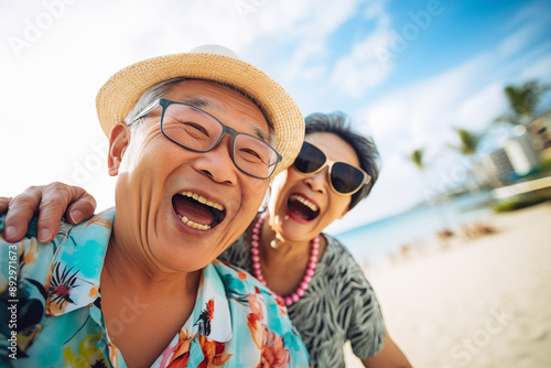 Asian senior couple on the beach, celebrating retirement, laughing together with glasses