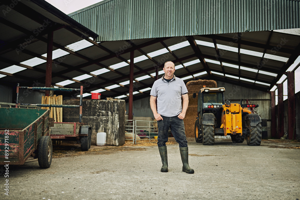 Fototapeta premium Agriculture, tractor and portrait of man in barn with equipment for farming, harvest and production. Farm, countryside and farmer with machine in shed, factory and storage with plow truck for fields